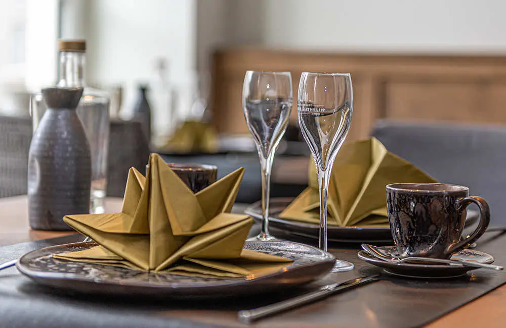 Gedekte ontbijttafel met goudkleurige gevouwen servetten, glazen en een koffietas