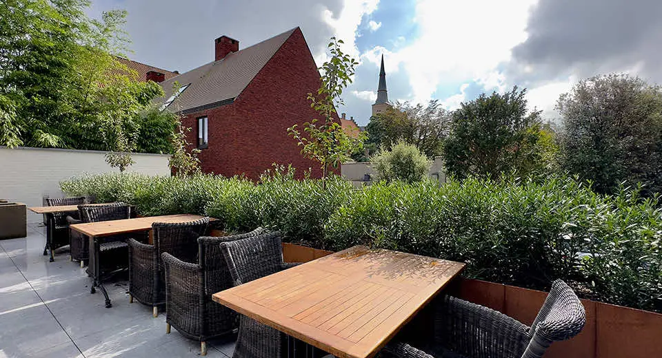 Terras met tafels en rieten stoelen, met zicht op de daken en een kerktoren