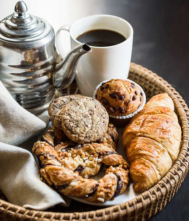 Mand met croissants, koeken en muffins naast een zilveren theepot en koffie