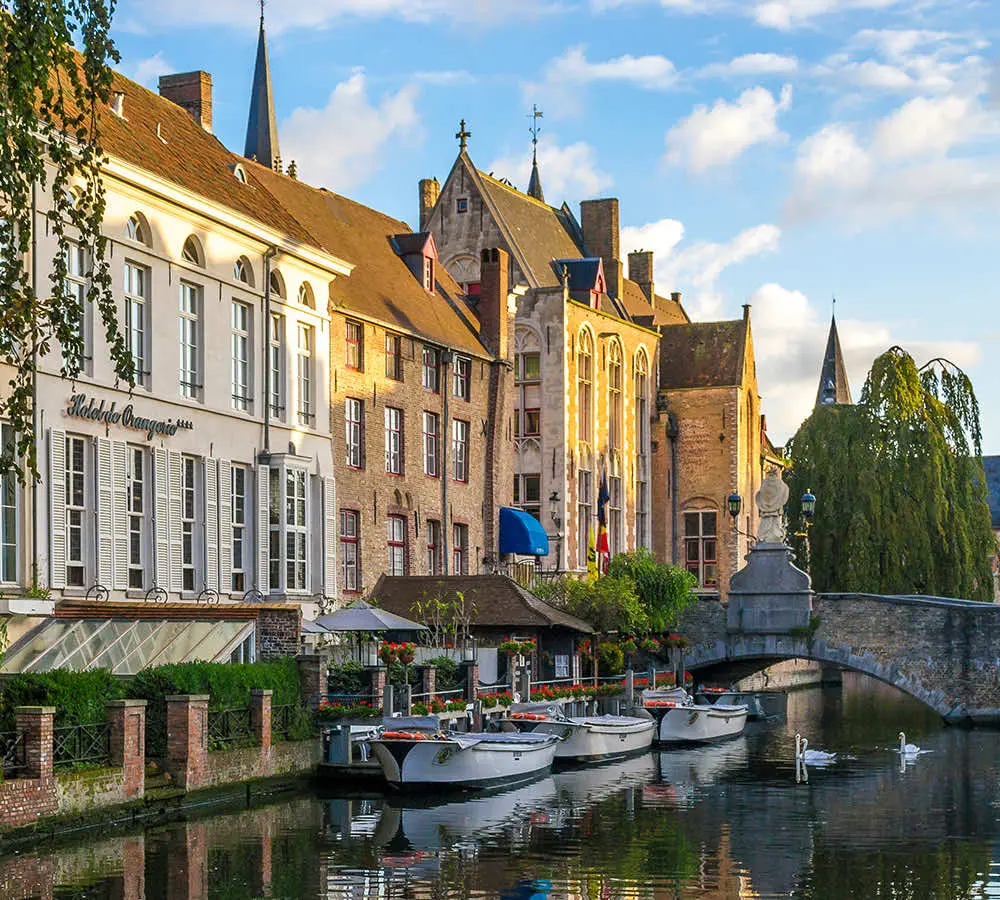 Historische gevels en aangemeerde rondvaartboten langs een Brugse rei