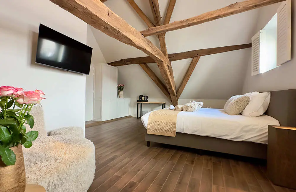 Suite met waterzicht: tweepersoonsbed en fauteuil onder de eiken dakspanten