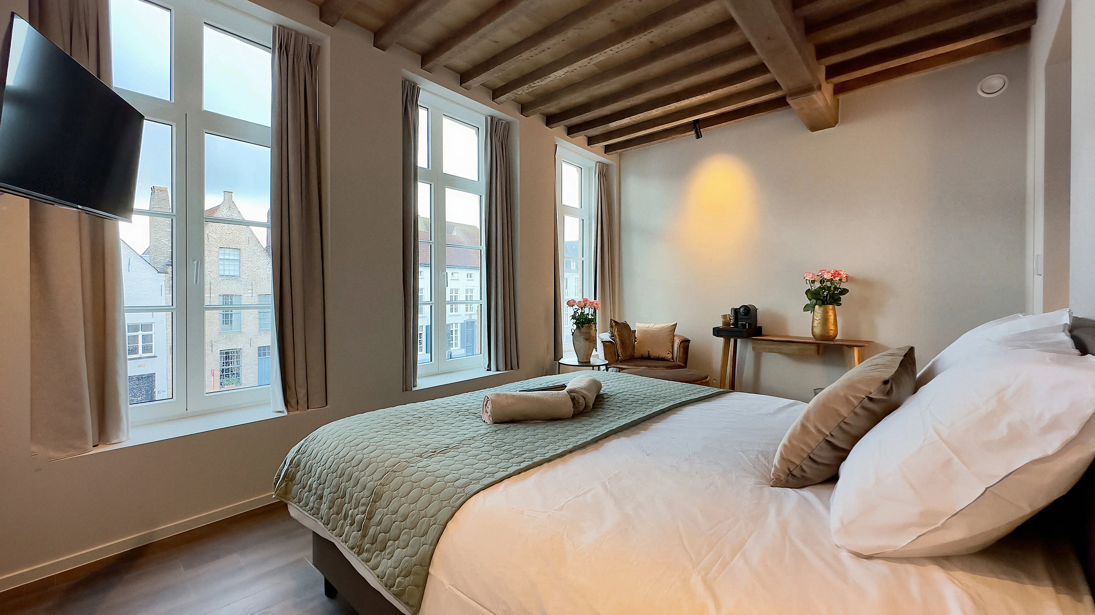 Deluxe kamer met tweepersoonsbed, groene sprei en hoge ramen onder het balkenplafond
